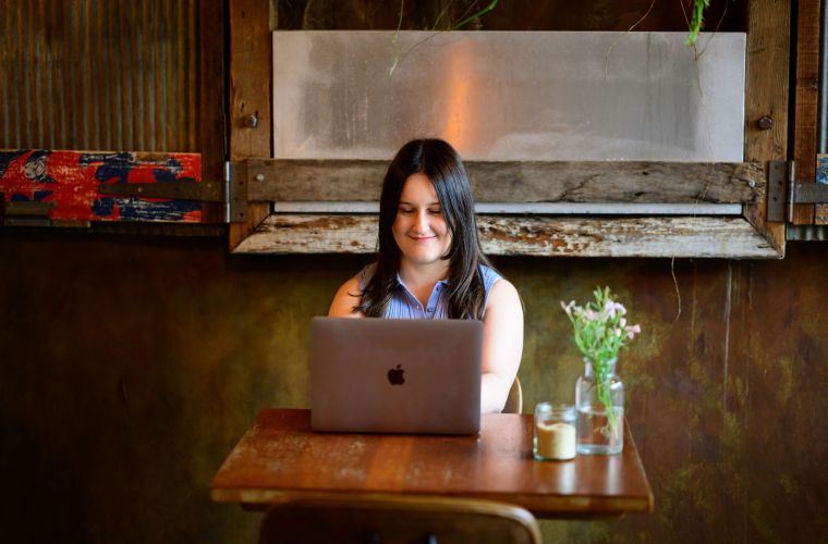 Copywriter Alex Haynes sitting at a cafe table, working on a laptop in front of her.